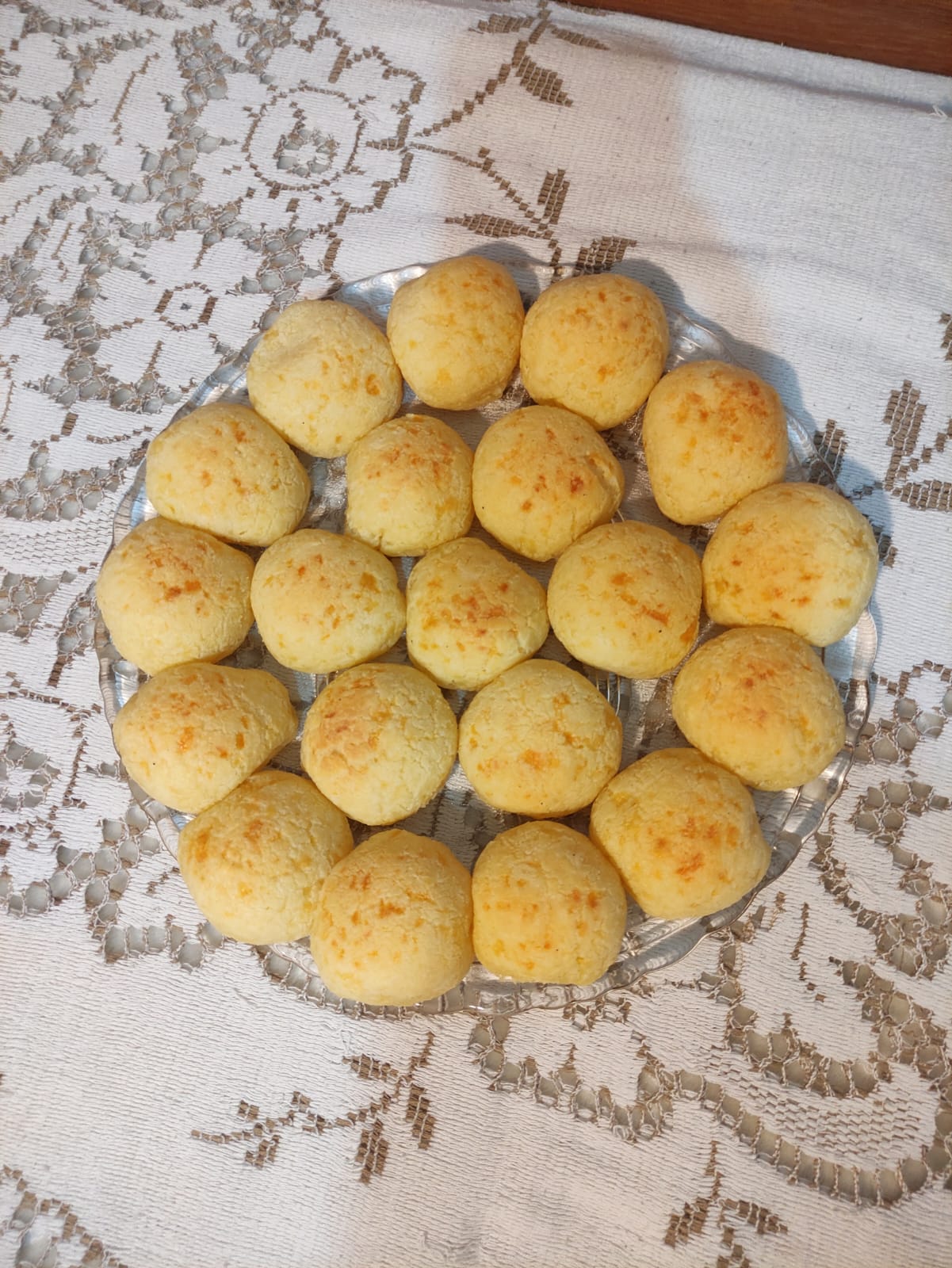 Pão de queijo dourado visto de cima sobre toalha de renda